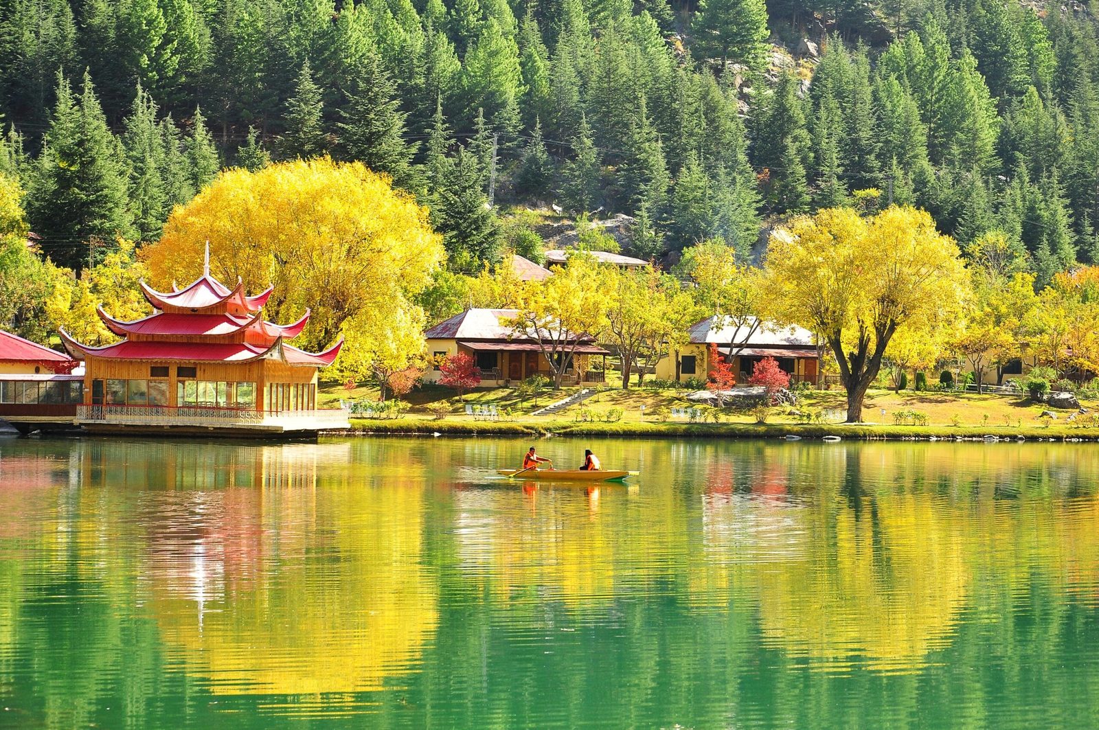 A small boat on the green water of Lower Kachura Lake with pine-covered slopes