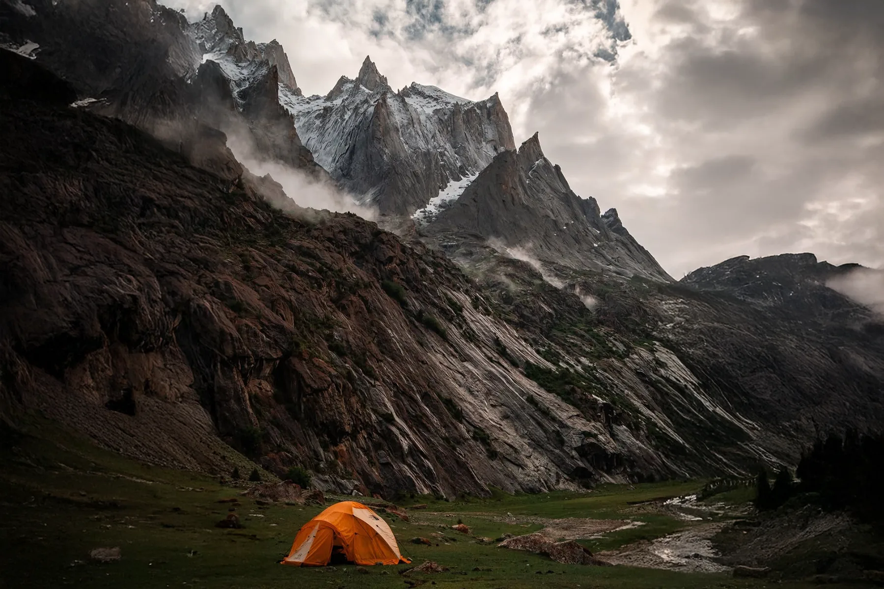 Orange expedition tent in a meadow below jagged rock spires