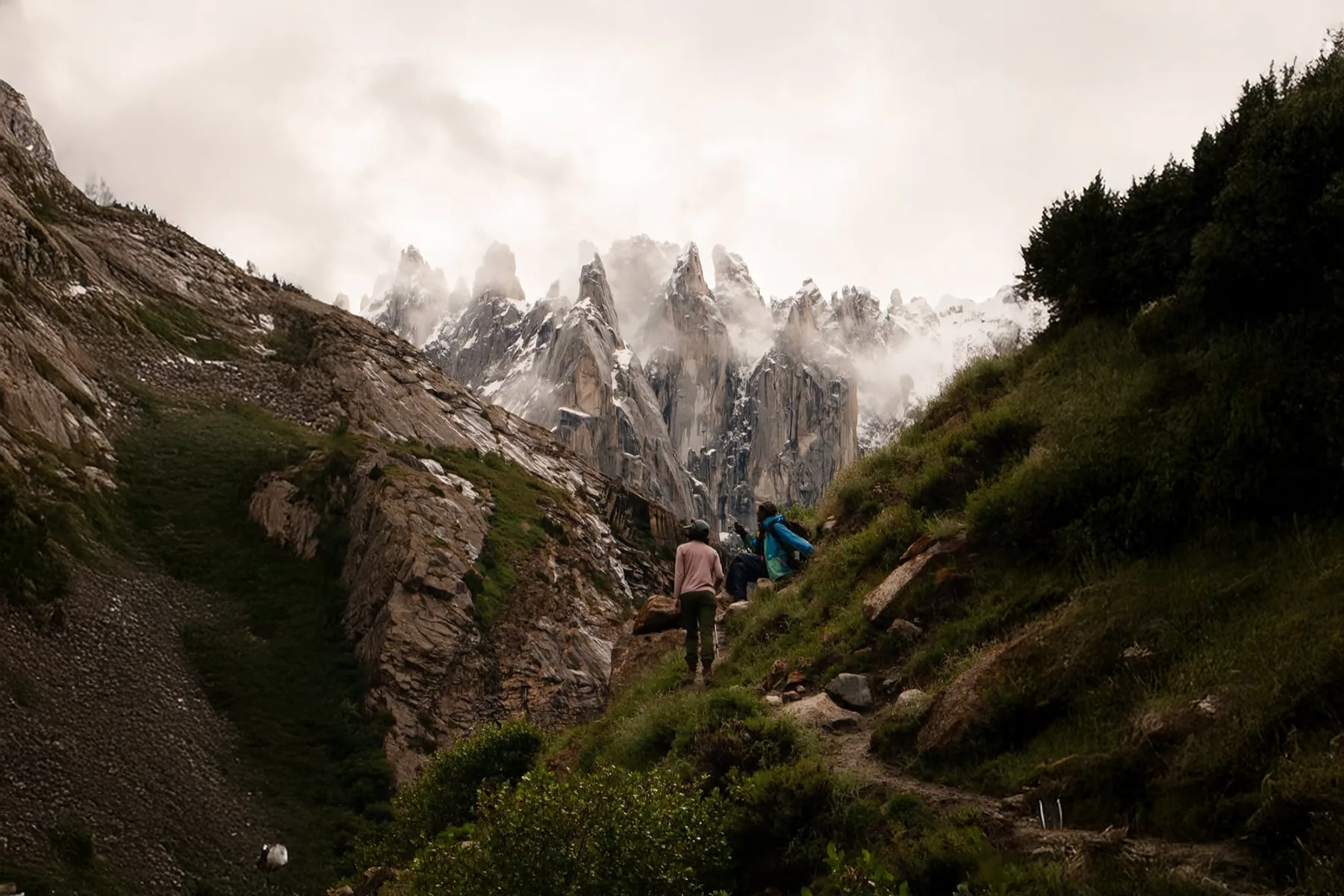 Trekkers on a green trail walking toward granite spires